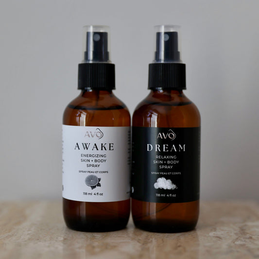 Left bottle facing forward is Avo's Awake Energizing skin and body spray made with Steam distilled organic essential oil blend with cold-pressed Lemon essential oil. Right bottle facing forward is Avo's Dream skin and Relaxing Spray made with Organic Simmondsia Chinensis (Jojoba) Oil Steam distilled organic essential oil blend